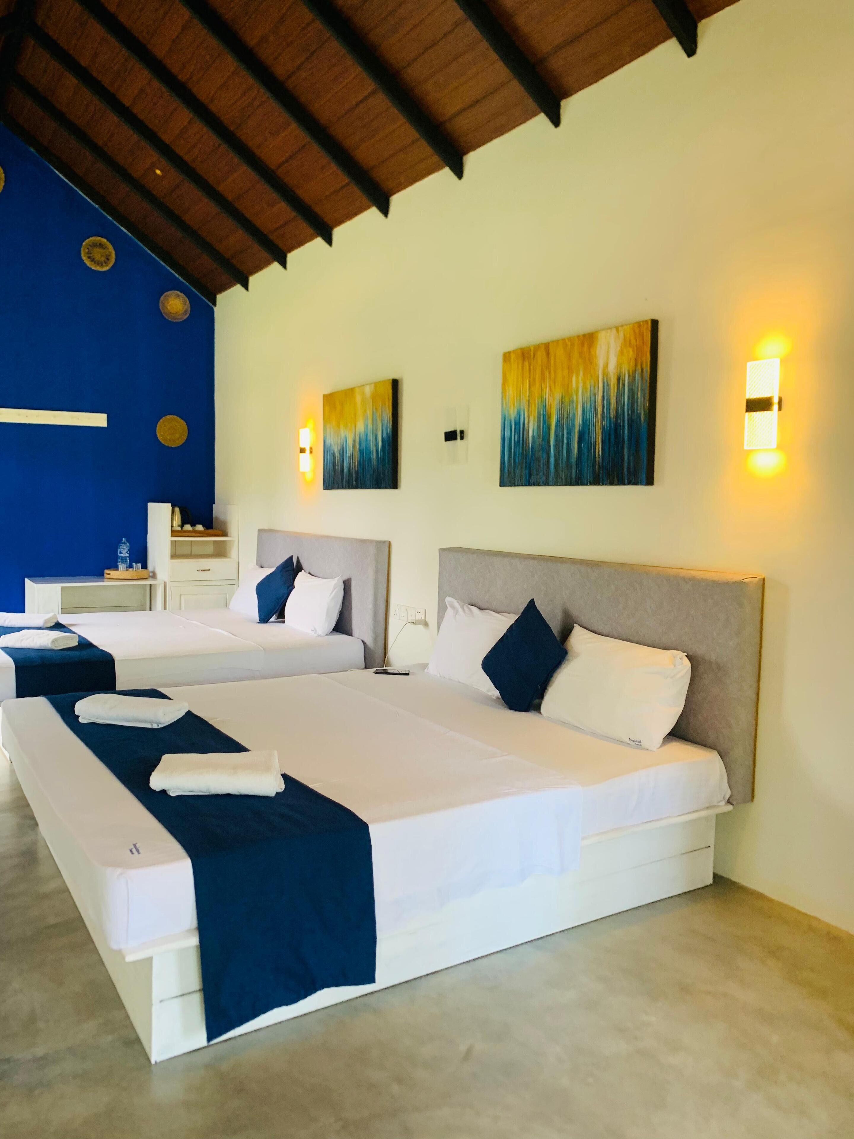 A hotel room with two beds, each with a headboard and pillows, a bedside table, and a wall-mounted light fixture.