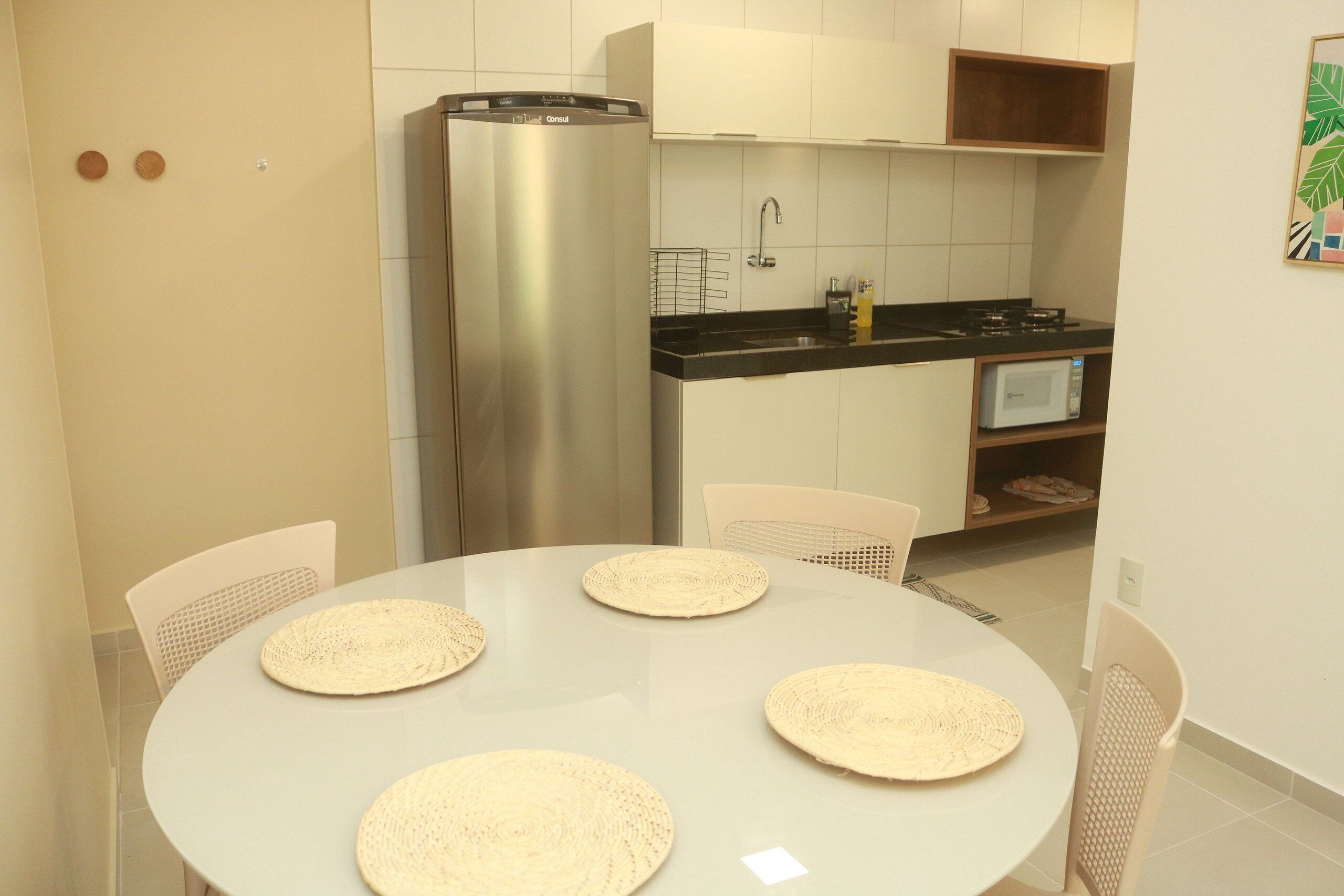 A modern kitchen with a stainless steel refrigerator, a microwave, and a sink. There are four woven placemats on a round table.