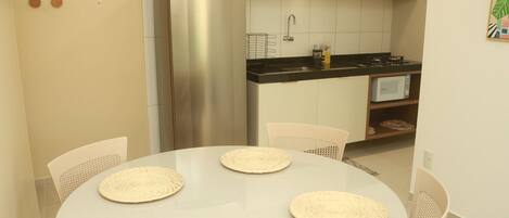 A modern kitchen with a stainless steel refrigerator, a microwave, and a sink. There are four woven placemats on a round table.