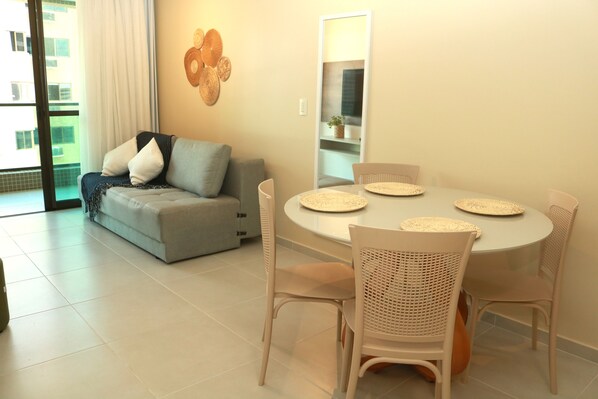 A modern living room with a grey sofa, white chairs, and a round dining table with woven placemats. - Smart Stay Ponta Verde Apt.603 (Maceió)