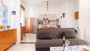 A modern living room with a sofa, a dining table with a patterned tablecloth, and a kitchen in the background. - Villa Immersed in Relaxation 500 Metres From the Sea (Avola)