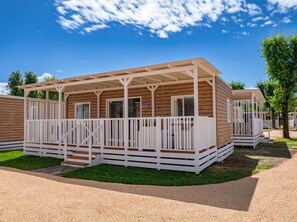 A row of wooden mobile homes with white railings and a gravel driveway.