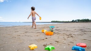 A child playing with toys on a sandy beach with a clear sky.