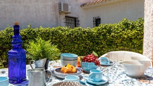 Une table dressée à l’extérieur, avec différents plats, une bouteille bleue et un pichet en métal.