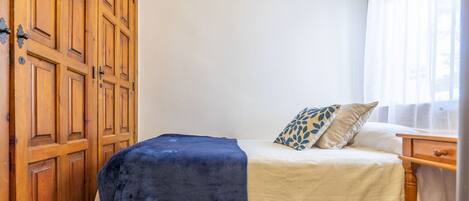 Une chambre à coucher comprenant un lit, une armoire en bois, une table de chevet et une fenêtre ornée de rideaux légers.