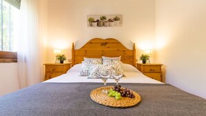 Un lit bien fait, recouvert d’une couverture grise, deux tables de chevet avec des lampes, une tête de lit en bois et une étagère à plantes fixée au mur.