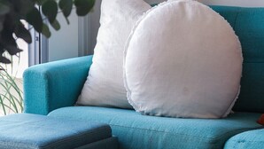 Un canapé de couleur turquoise agrémenté de deux coussins blancs et d’un pouf assorti. Un livre est posé sur la table devant le canapé.