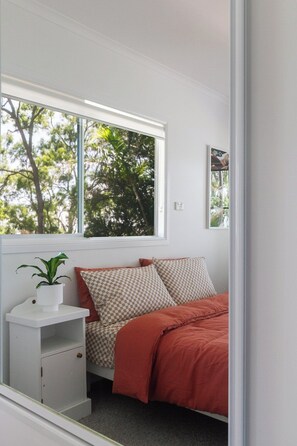 A bedroom with a bed, a window, a bedside table with a plant, and a wall-mounted picture. - The Lakehouse - absolute waterfront retreat (Wooloweyah)