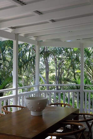 A covered outdoor area with a table and chairs, surrounded by a white railing, overlooking a tropical garden. - The Lakehouse - absolute waterfront retreat (Wooloweyah)