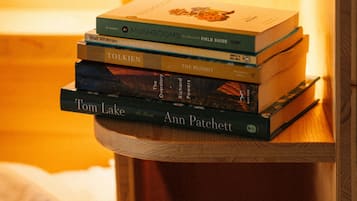 A stack of books on a wooden nightstand with a white mug beside it.