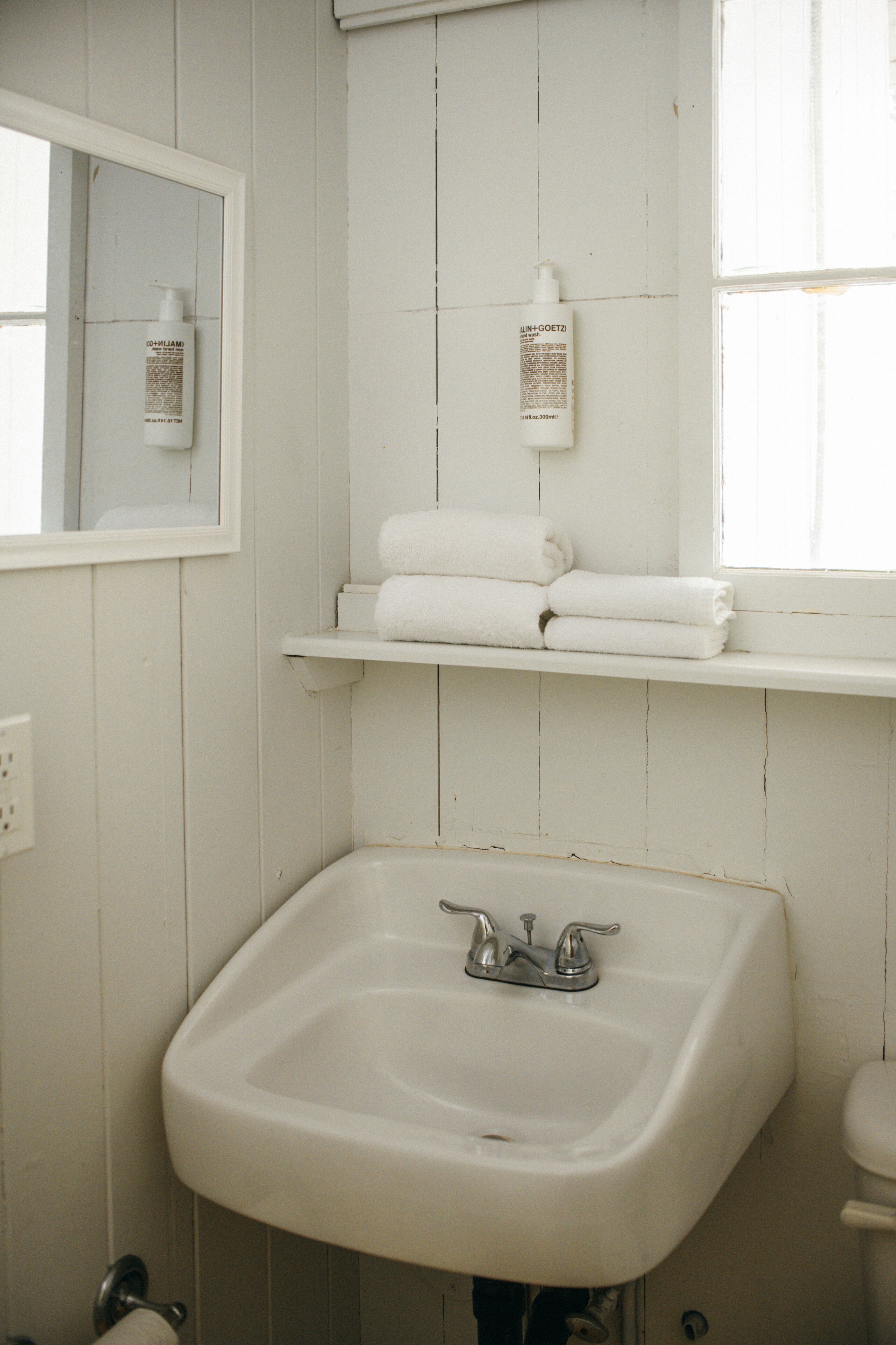 Un baño con un lavabo blanco, un espejo y una repisa con toallas dobladas.
