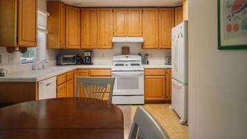 Una cocina con armarios de madera, una estufa blanca, un refrigerador y una mesa de comedor con sillas.