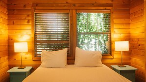 Una habitación de cabaña de madera con una cama, dos lámparas de noche y ventanas con persianas.