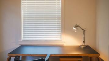 Ein Schreibtisch mit Stuhl, einer Lampe und einem Fenster mit Jalousien.