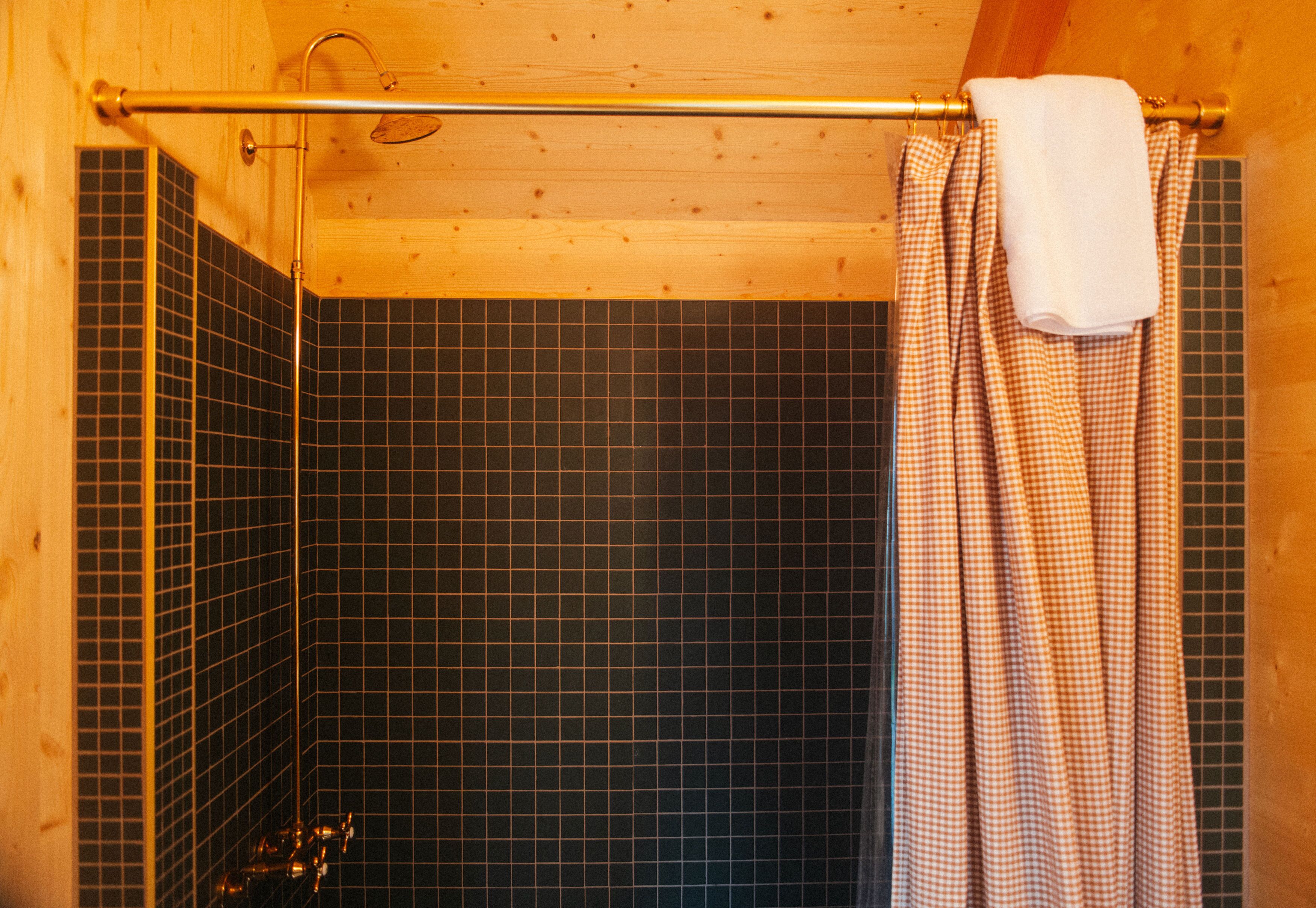 Douchegedeelte met betegelde muur, een metalen douchekop en een zwart-wit geblokt douchegordijn.