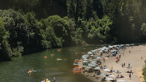 Una playa junto al río, con barcos, sombrillas y gente.