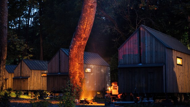 Una cabaña rústica con chimenea en el centro, rodeada de árboles.