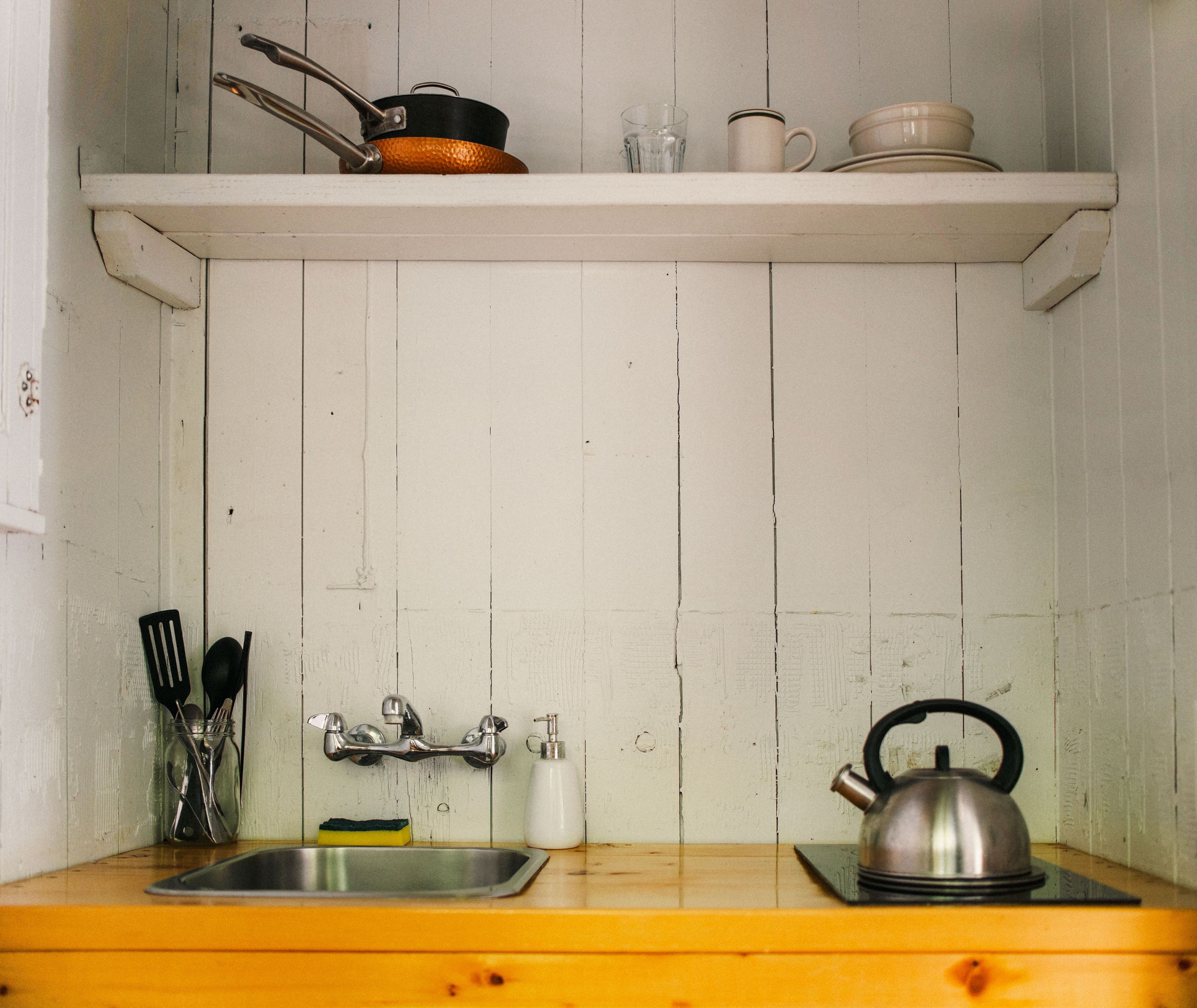 Una cucina con un piano di lavoro in legno, un lavello in acciaio inossidabile, un bollitore e una mensola sopra con un bollitore, una tazza e una pentola.