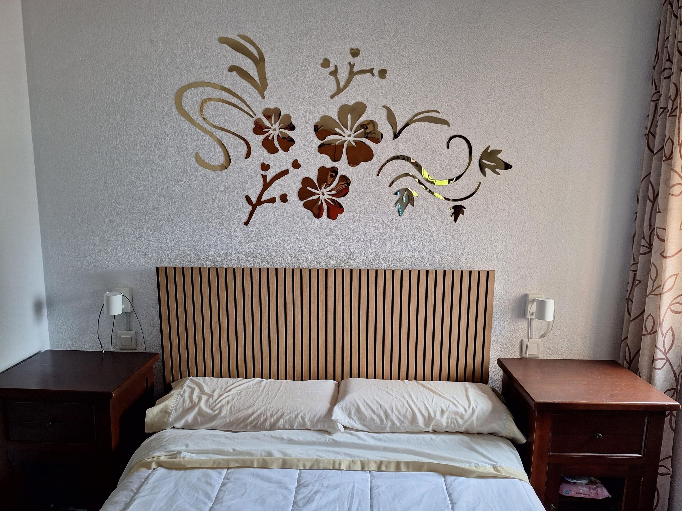 Hotellihuone, jossa on sänky, kaksi yöpöytää, seinään kiinnitetty valaisin ja koristeellinen kukkatapetti.