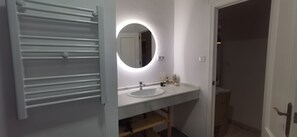 Ein Badezimmer mit Waschbecken, Spiegel mit runder Beleuchtung und Handtuchhalter.