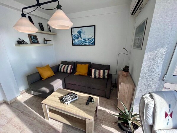 A modern living room with a sofa, a coffee table, and a floor lamp. There is a framed artwork on the wall and a small shelf with decorative items.