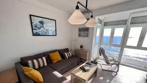 Ein modernes Wohnzimmer mit grauem Sofa, Couchtisch aus Holz und Meerblick durch große Fenster.