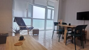 Ein modernes Zimmer mit Holztisch, Stühlen, einem Fernseher und Meerblick durch große Fenster.