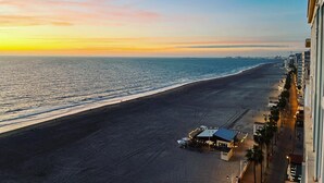 Blick auf einen Strand, mit einem Gebäude rechts und einem Sonnenuntergang im Hintergrund.