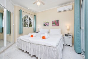 Une chambre d’hôtel avec un lit, une table de chevet, une fenêtre avec des rideaux et un ventilateur de plafond.