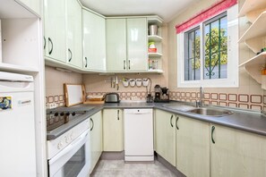 Une cuisine compacte équipée d’une cuisinière, d’un lave-vaisselle et d’une fenêtre donnant sur un espace verdoyant.