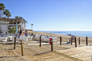 Een restaurant aan het strand met terras en een houten vlonder naar het zand.