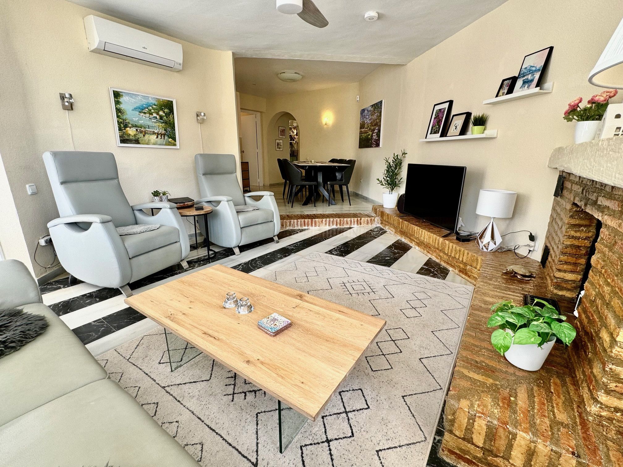 Ein modernes Wohnzimmer mit Couchtisch aus Holz, grauen Sesseln, einem Fernseher und einem Kamin.