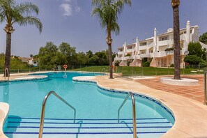 A swimming pool with a curved design, surrounded by palm trees and a building with balconies.