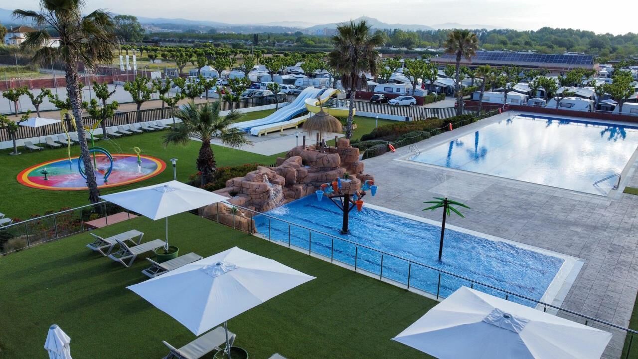 Ein Schwimmbecken mit Wasserrutsche und Felsformation, umgeben von Liegestühlen und Sonnenschirmen.
