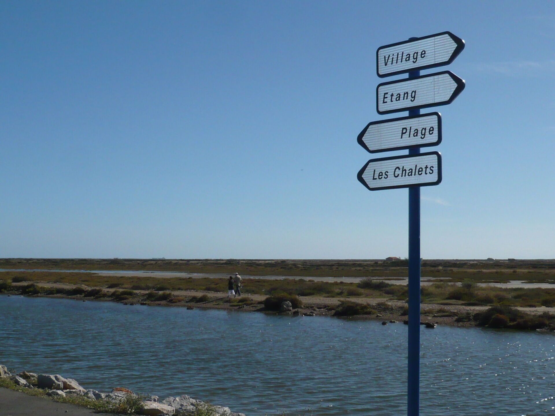 Un panneau indicateur avec des flèches pointant vers « Village », « Étang », « Plage » et « Les Chalets ».