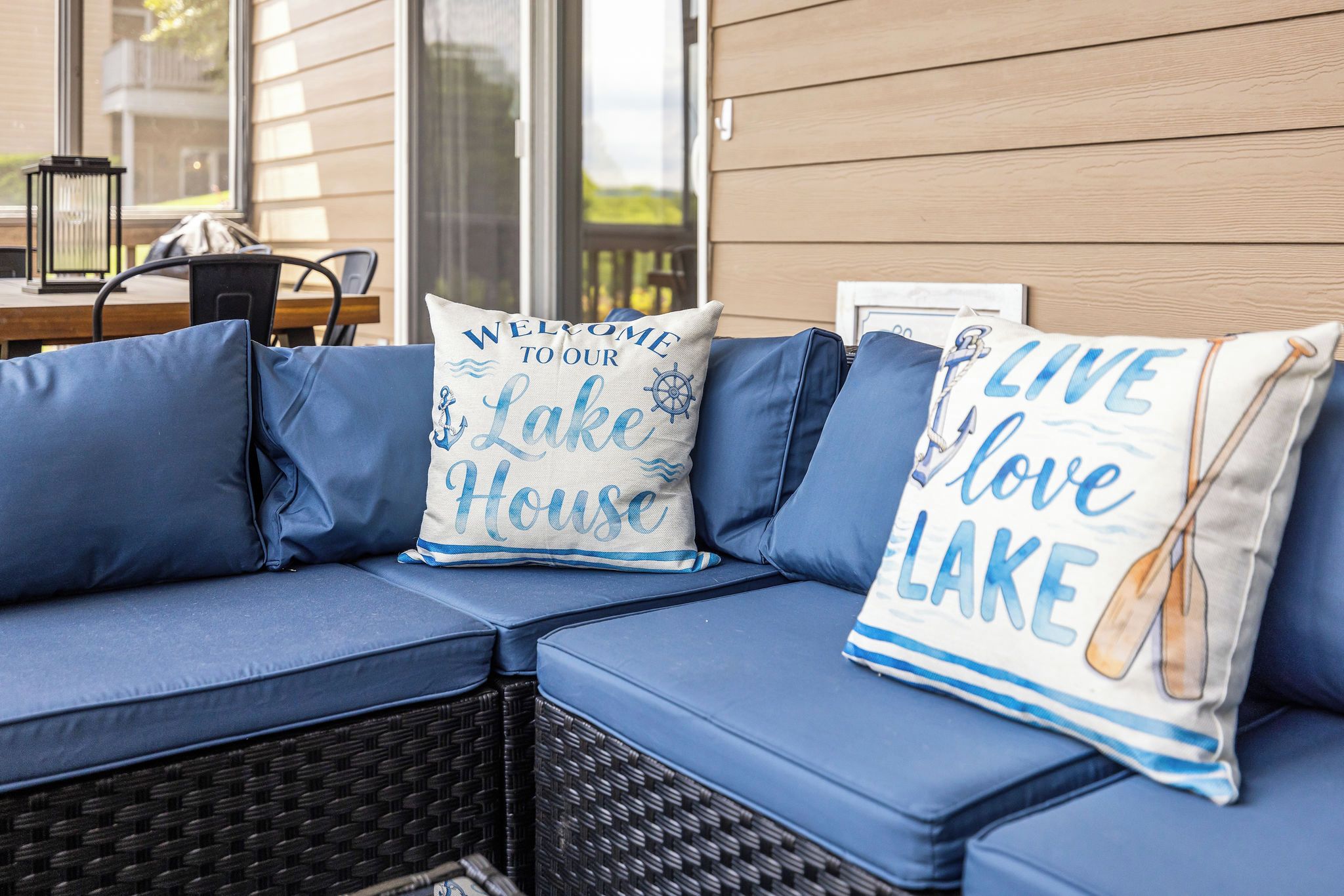 A blue sofa with cushions, a wicker chair, and a table with a lantern.