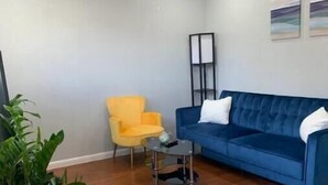 A living room with a blue sofa, a yellow armchair, a glass coffee table, a ceiling fan, and a potted plant. - Cozy, Convenient, Modern update (Gonzales)