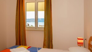 A hotel room with a bed, a window with curtains, a bedside table with a lamp, and a view of the sea. - Lovely apartment for 4 people with WIFI, A/C, TV and terrace (Senj)