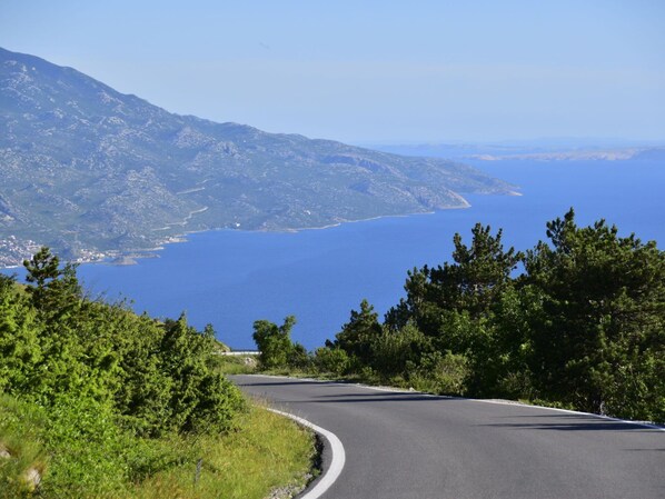 A winding road curving through a mountainous landscape with a view of a large body of water.