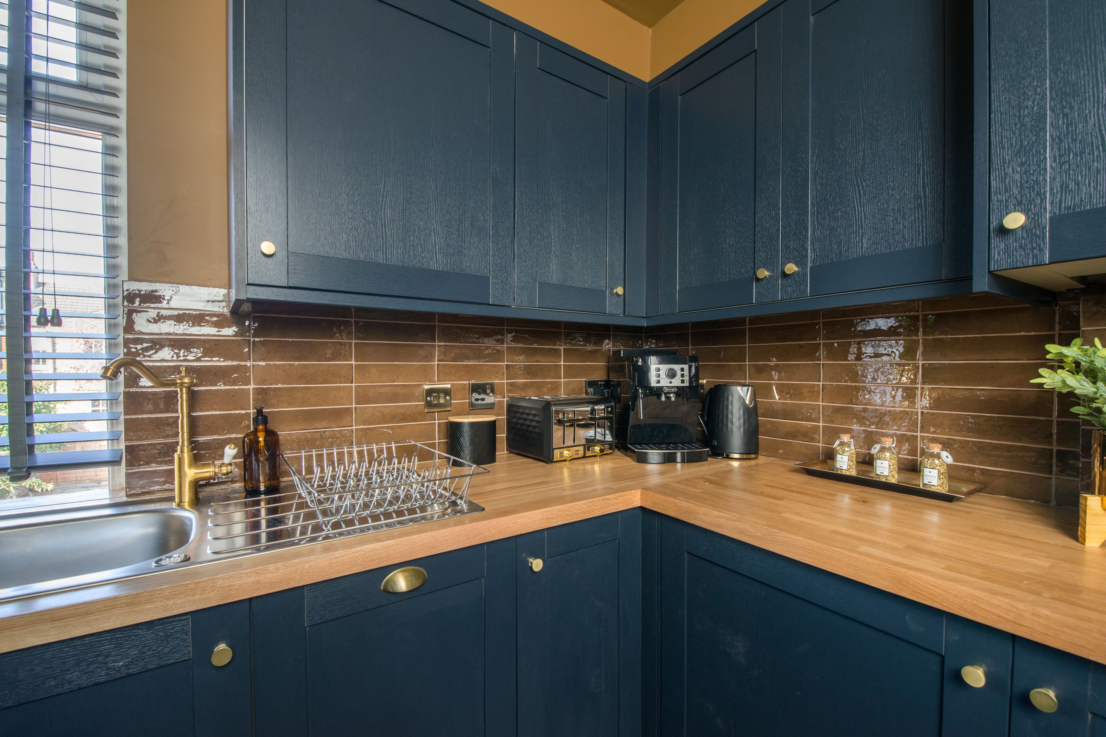 A kitchen with dark blue cabinets, a wooden countertop, a coffee maker, and a dish rack.
