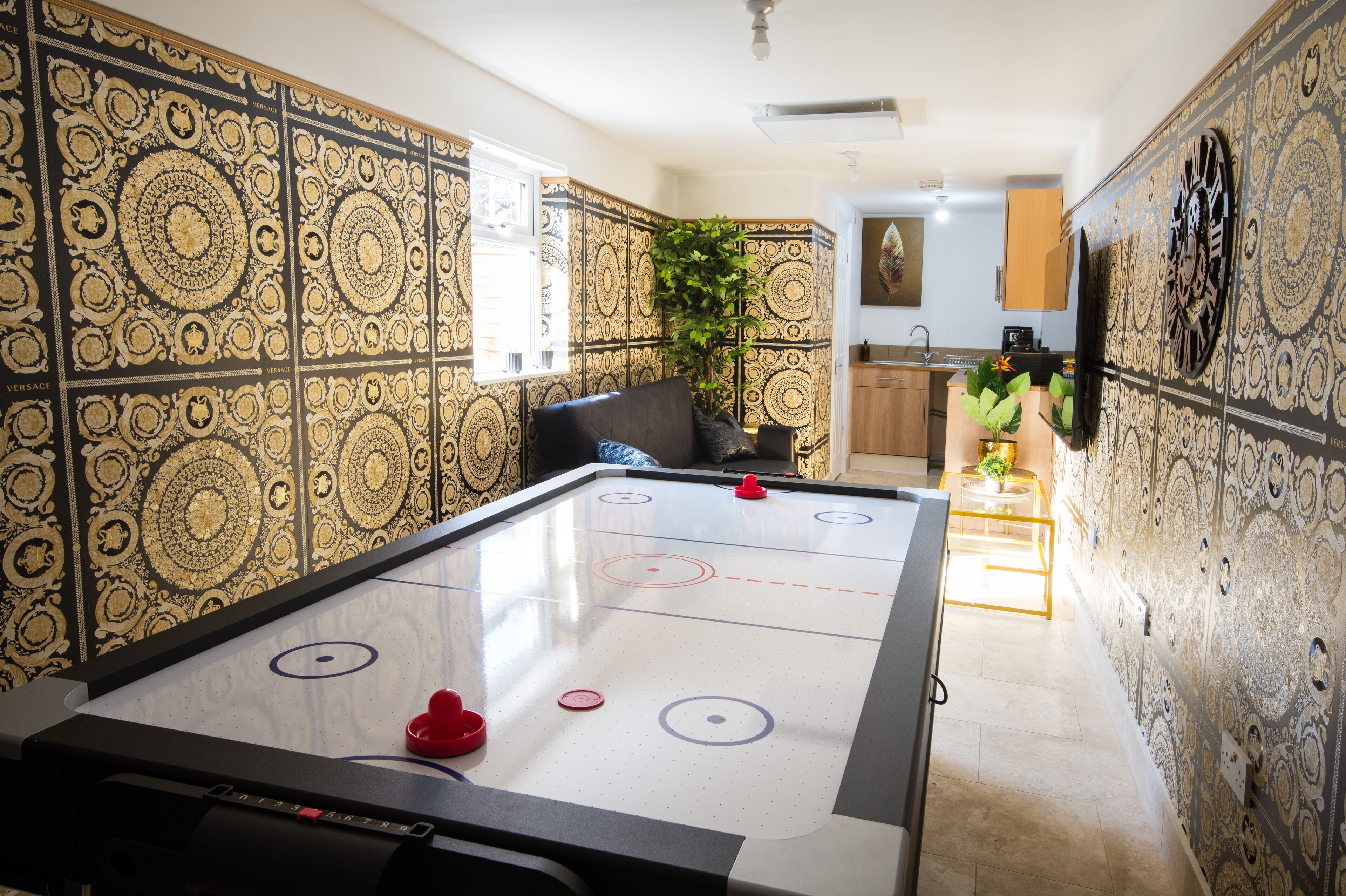 A room with a shuffleboard table, a potted plant, and patterned wallpaper.