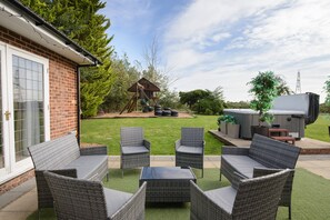 A patio with wicker furniture, a hot tub, and a wooden playhouse.