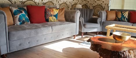 A living room with a grey sofa, armchairs, and a coffee table with a wooden base.