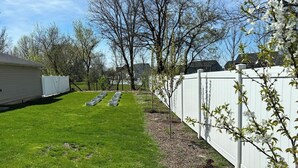 Un jardin avec une clôture blanche, une pelouse et des arbres.