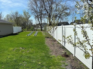 Un jardin avec une clôture blanche, une pelouse et des arbres.