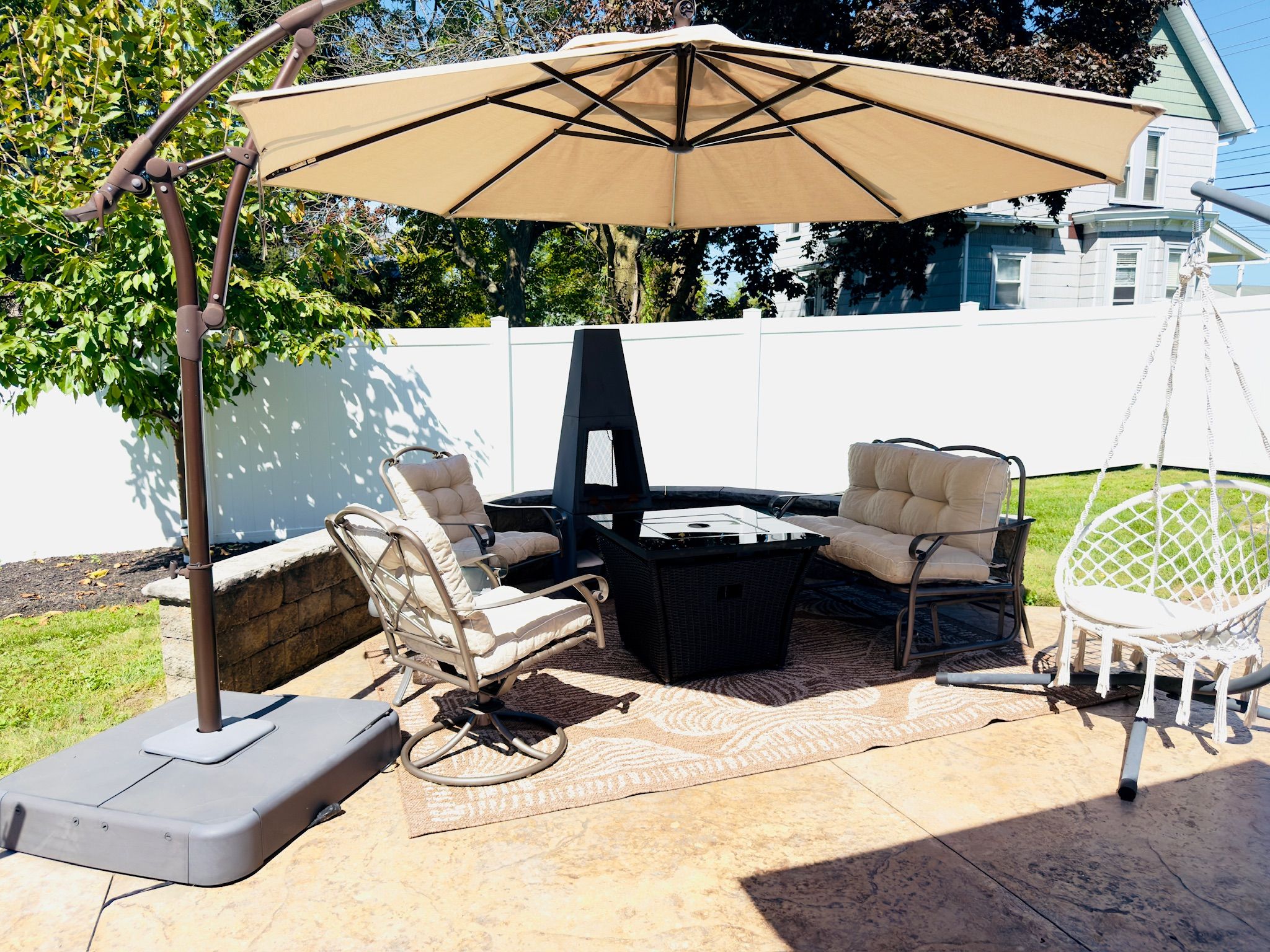 Eine Terrasse im Freien mit Tisch, zwei Stühlen und einer Hängematte, beschattet von einem großen Sonnenschirm.