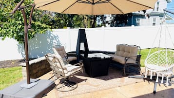 Eine Terrasse im Freien mit Tisch, zwei Stühlen und einer Hängematte, beschattet von einem großen Sonnenschirm.