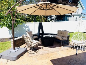 Eine Terrasse im Freien mit Tisch, zwei Stühlen und einer Hängematte, beschattet von einem großen Sonnenschirm.