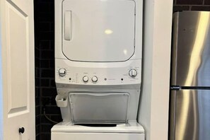 Cocina compacta con lavadora y secadora integradas, refrigerador de acero inoxidable y una puerta con manija.