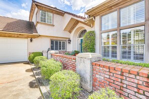 A two-story house with a garage, a brick wall, and a small garden area with bushes and a potted plant. - Escondido Home: Private Pool, 2 Grills & Fire Pit! (Escondido)